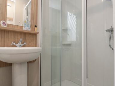 A bathroom with a pedestal sink a mirror a wooden shelf a shower cubicle with glass doors and a handheld shower at Rowan Court 2 in Cayton