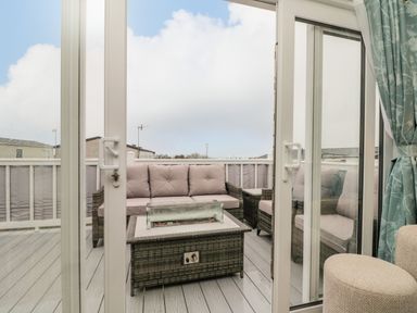 A deck area with wicker sofa and chairs around a fire pit table seen through sliding glass doors at Rowan Court 2 in Cayton