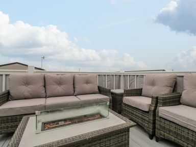 An outdoor seating area with cushioned wicker sofa and chairs around a table with a glass fire pit at Rowan Court 2 in Cayton