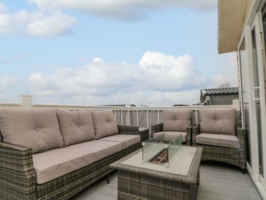 An outdoor seating area with a sofa, two chairs, and a glass-covered fire pit table at Rowan Court 2 in Cayton