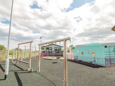 A playground with wooden climbing structures and a teal shipping container with food images at Rowan Court 2 in Cayton