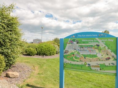An outdoor area with a signboard showing a map of Cayton Bay Holiday Park surrounded by bushes and grassy lawn at Rowan Court 2 in Cayton