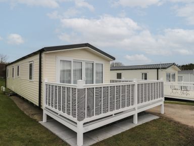 A beige mobile home with a white and grey fenced porch on a grassy area at Rowan Court 2 in Cayton