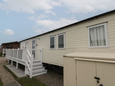 An exterior view of a beige mobile home with a white ramp and stairs and a storage box at Rowan Court 2 in Cayton