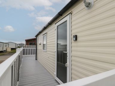 Exterior side view of a beige mobile home with a white door and window and a gray deck with white railing at Rowan Court 2 in Cayton