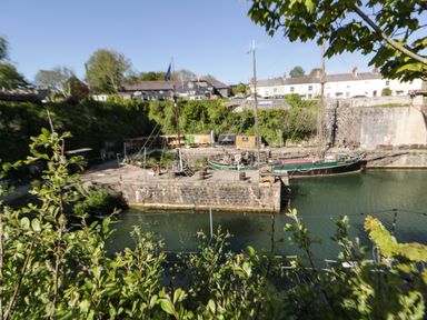 A dock with a moored sailing ship surrounded by stone walls and buildings at Sea View in St Austell