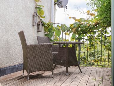 An outdoor balcony with two wicker chairs and a wicker table with climbing plants on the railing at Sea View in St Austell