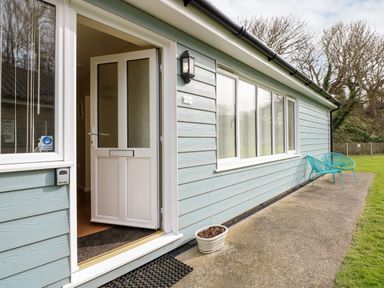 An open white door leading into a house with blue siding two blue chairs on a concrete path and grass at 1 The Dell in Mundesley
