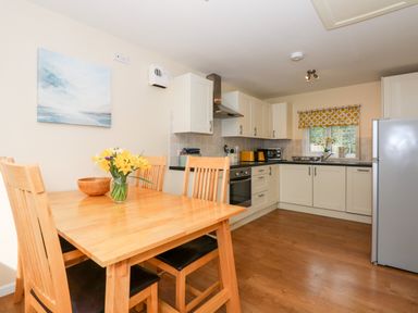 A kitchen with wooden dining table and chairs white cabinets and a refrigerator at 1 The Dell in Mundesley