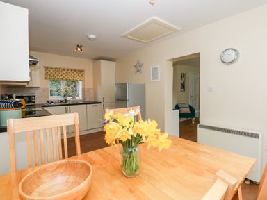 A kitchen with wooden dining table and chairs and a vase of yellow flowers at 1 The Dell in Mundesley