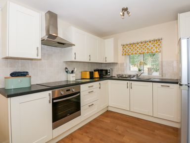 A kitchen with white cabinets black countertop oven microwave and window with yellow patterned blind at 1 The Dell in Mundesley