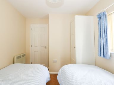 A bedroom with two single beds a white wardrobe a door and a window with blue curtains at 1 The Dell in Mundesley