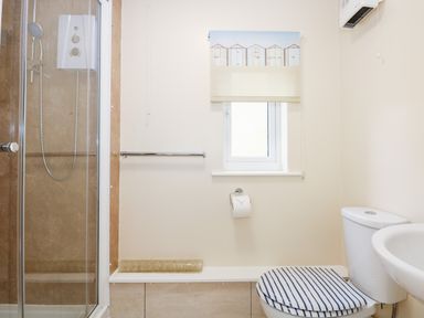A bathroom with a shower enclosure a toilet with a striped seat cover and a sink at 1 The Dell in Mundesley