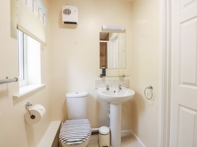 A bathroom with a toilet, pedestal sink, mirror, window, and wall-mounted heater at 1 The Dell in Mundesley
