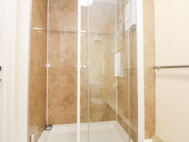 A shower enclosure with glass doors and beige walls next to a towel rail at 1 The Dell in Mundesley