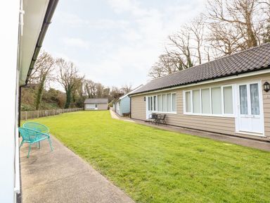 A row of single-story houses with patios and chairs along a grassy yard at 1 The Dell in Mundesley
