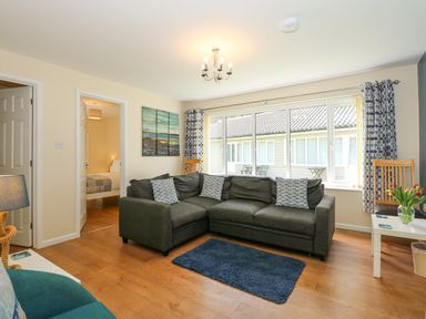 A living room with a dark grey sectional sofa and patterned cushions at 1 The Dell in Mundesley