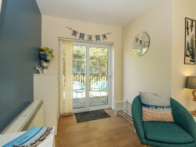 A seating area with a chair and cushion near sliding glass doors with a sign above saying BEACH at 1 The Dell in Mundesley