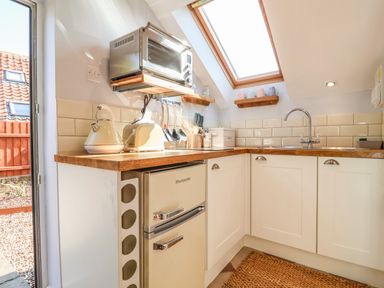 A kitchen with wooden countertops white cabinets a small fridge toaster kettle microwave and a skylight window at Admiral Cottage in Blaxhall near Snape Suffolk