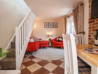A living room with a red sofa and armchair a round rug and a dining table with white chairs at Admiral Cottage Blaxhall near Snape Suffolk