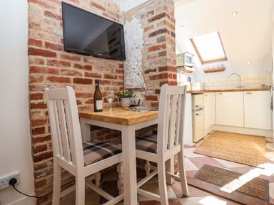 A small dining table with two chairs next to a brick wall and a kitchen with skylight at Admiral Cottage Blaxhall near Snape Suffolk