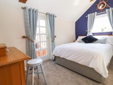 A bedroom with a bed desk stool and striped curtains at Admiral Cottage in Blaxhall near Snape Suffolk