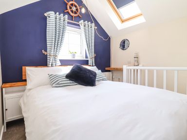 A bedroom with a bed with white linens and striped pillows under a window with striped curtains at Admiral Cottage in Blaxhall near Snape Suffolk
