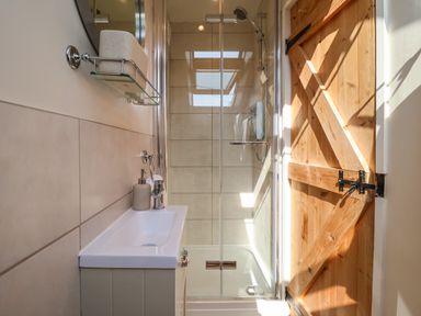 A small bathroom with a shower, sink, soap dispenser, and wooden door at Admiral Cottage Blaxhall near Snape Suffolk