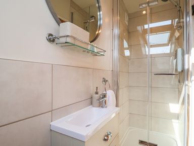A bathroom with a sink a mirror a glass shelf and a glass door shower at Admiral Cottage in Blaxhall near Snape Suffolk