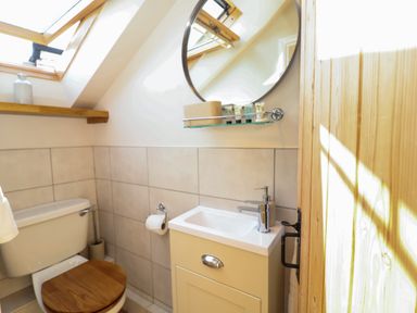 A bathroom with a toilet wooden seat sink with faucet round mirror and wooden door at Admiral Cottage Blaxhall near Snape Suffolk