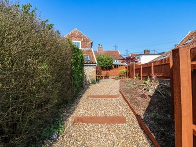 Gravel pathway with wooden borders and small plants next to fences and bushes at Admiral Cottage in Blaxhall near Snape Suffolk