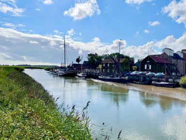 A river with boats moored along a quay with buildings and parked cars nearby at Admiral Cottage in Blaxhall near Snape Suffolk