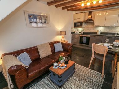 A living area with a brown leather sofa next to a small wooden table and an open kitchen with dining table and chairs at Mulberry Tree in Appledore