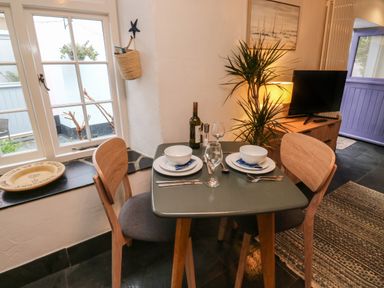 A dining table set for two with plates bowls glasses and cutlery next to a window and a plant in a room at Mulberry Tree in Appledore