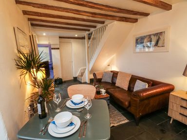 A living room with a dining table set for two a brown leather sofa plants and exposed wooden beams at Mulberry Tree in Appledore