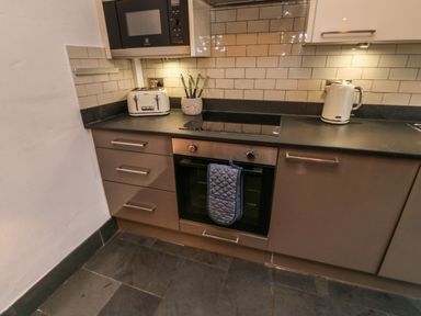 A kitchen countertop with a microwave, toaster, knife holder, electric kettle, stovetop, oven with a hanging mitt and tiled backsplash at Mulberry Tree in Appledore