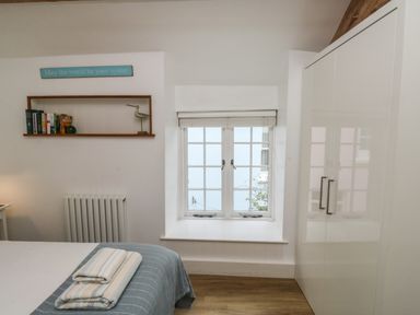 A bedroom with a bed and folded towels a window a white wardrobe and a wall shelf with books and a decorative bird at Mulberry Tree in Appledore