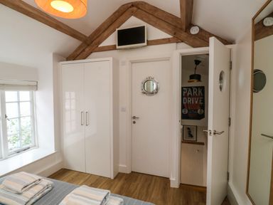 A bedroom with a bed with folded towels a white wardrobe a door with a porthole window and wooden ceiling beams at Mulberry Tree in Appledore