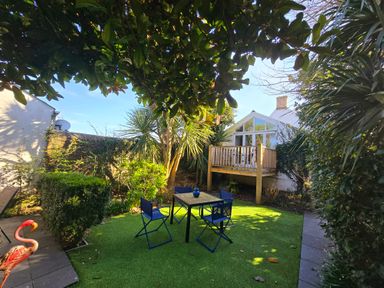 A garden area with blue chairs and a table on artificial grass and a wooden deck attached to a white house at Mulberry Tree in Appledore