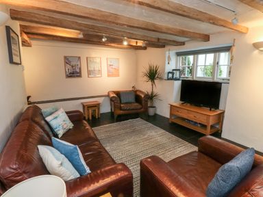 A living room with leather sofas and armchairs a television on a wooden stand and a plant at Pear Tree Cottage in Appledore