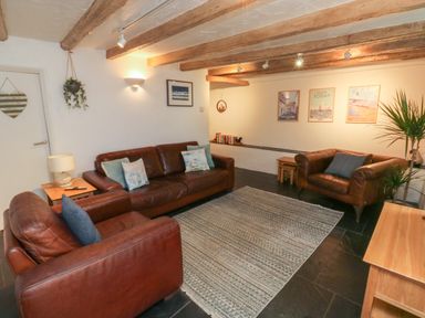 A living room with leather sofas a rug wooden beams on the ceiling and framed pictures on the wall at Pear Tree Cottage in Appledore