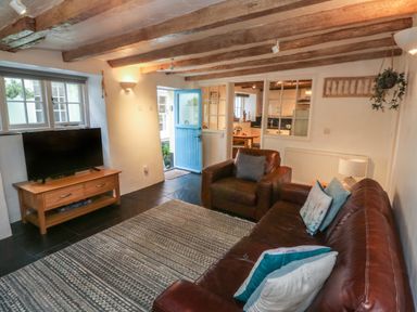 A living room with leather sofa and armchair a wooden TV stand with a television and a blue door at Pear Tree Cottage in Appledore