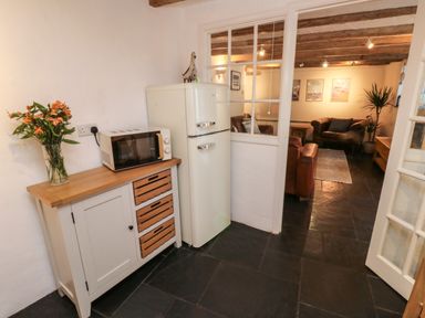 A kitchen area with a microwave on a cabinet and a refrigerator next to a living room with sofas and framed pictures on the wall at Pear Tree Cottage in Appledore