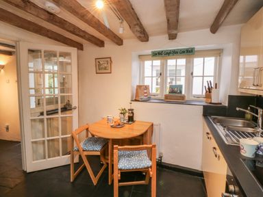 A kitchen with a wooden table and chairs next to a window and a sink on the counter at Pear Tree Cottage Appledore