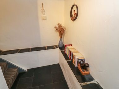 A small hallway corner with black tiled ledges holding books a vase with dried plants and a small decorative sculpture at Pear Tree Cottage in Appledore
