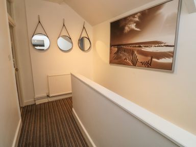 A narrow hallway with three round mirrors on the wall and a large framed beach scene at Pear Tree Cottage in Appledore
