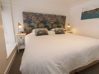 A bedroom with a large bed two bedside tables with lamps and a painting on the wall at Pear Tree Cottage in Appledore