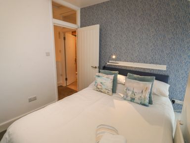 A bedroom with a double bed with pillows and a partially open door at Pear Tree Cottage in Appledore