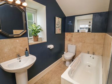 A bathroom with a bathtub toilet and sink with a window and a plant at Pear Tree Cottage in Appledore