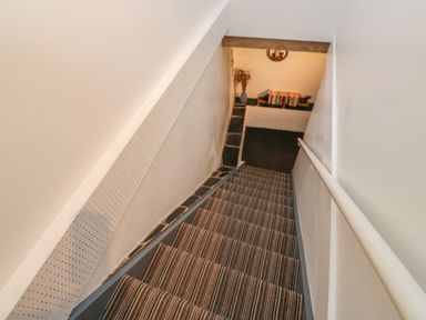 Narrow staircase with striped carpet leading down to a small landing with books and a vase at Pear Tree Cottage in Appledore